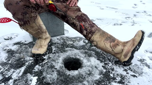 Ice fishing on frozen lake. Catching fish through an opening in the ice on a frozen body of water. Catching fish in a hole in the ice on frozen river. Winter fishing. Jigging with Small jigging rod. 