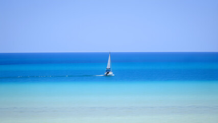 Obraz premium A small boat drifting peacefully in the middle of the vast ocean, surrounded by endless blue water and a clear sky. A serene and tranquil scene that evokes a sense of solitude.