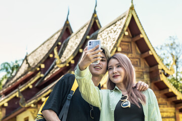 Young Asian tourist couples using phone selfie during summer vacation in Thailand temple