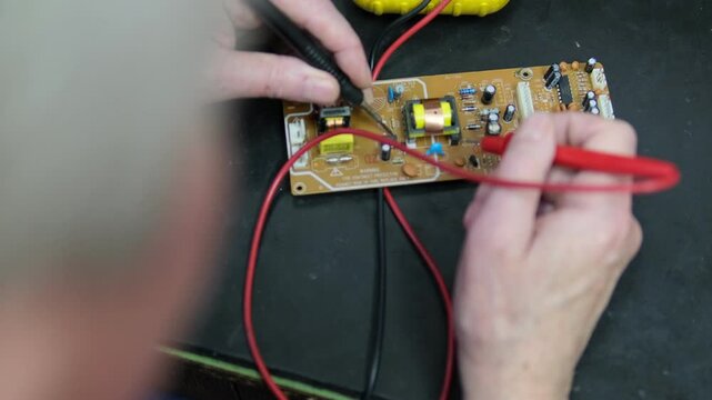Hands of an electrician using a multimeter to test a circuit board, checking voltage and diagnosing components.