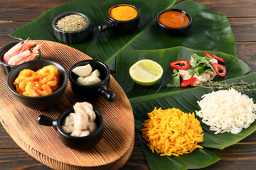 Cut banana leaves with different food, board, spices and sauce on wooden table, closeup
