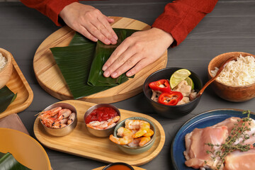 Woman wrapping food into banana leaf at wooden table with products, closeup. Healthy eco serving