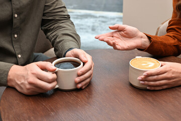 Colleagues having coffee break at wooden table in cafe, closeup