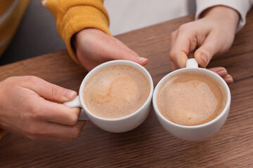 Coffee break. Women with cups of hot drinks at wooden table indoors, closeup