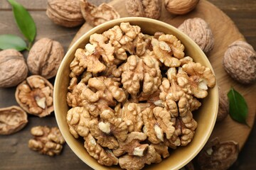 Peeled walnuts in bowl and whole ones on table, flat lay