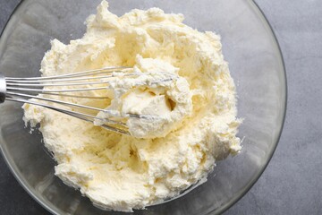 Bowl with whisk and whipped cream on grey table, top view
