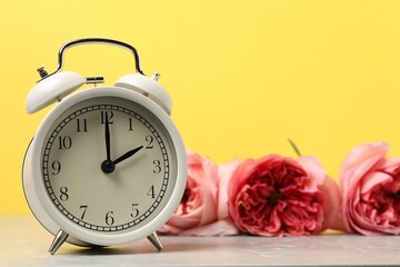 Spring time. Alarm clock and beautiful flowers on grey marble table against yellow background,...