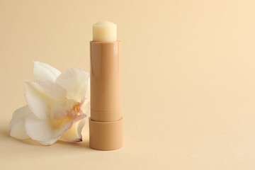 Lip balm and flower on beige background, closeup. Space for text