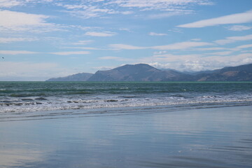 A beautiful beach in New Zealand with gentle ocean waves, soft sand, and distant mountains under a clear sky. A perfect destination for relaxation and coastal exploration.