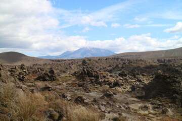 Vast volcanic landscape in New Zealand with rugged terrain, scattered rocks, and distant mountains under a bright blue sky. A dramatic and remote setting ideal for adventure and exploration themes.