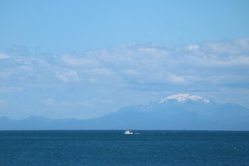 A serene ocean view with a distant snow-capped mountain and a lone boat sailing under a vast blue sky. Perfect for travel, adventure, and exploration themes, evoking freedom and tranquility.