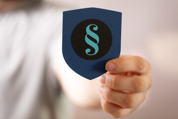 Image of a hand holding a shield with a paragraph symbol, representing legal protection and...