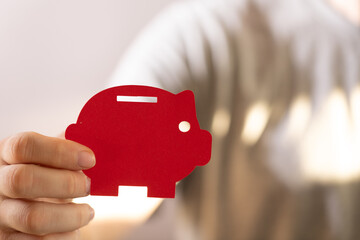 Close-up of a hand holding a red piggy bank cutout.  Concept for saving money, finance, and...