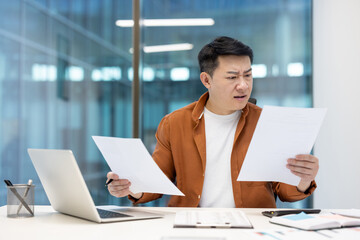 Upset and worried financier looking and reading negative financial reports. Asian nervous man...