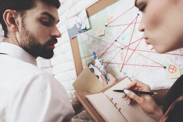 Private detective agency. Man and woman are looking at map, discussing clues.