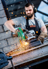 Industrial worker cutting metal with many sharp sparks working on compound mitre saw with circular blade