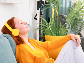 Woman with yellow headphones and a glass of wine sitting on the sofa at home and listening to music or podcast. music and relaxation