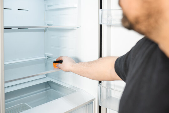 Man cleans up  a refrigerator shelf. Kitchen chores. Man cleaning fridge with sponge.