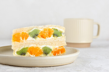 Half sandwiches bread stuffed with mascarpone cream cheese, kiwi, orange and cup of tea. Homemade Korean dessert.
