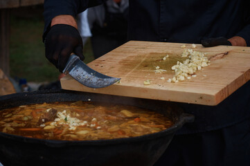 The chef adds garlic chopped on a cutting board to the meat soup with a knife. Boiling fresh food from vegetables and beef in a large cauldron. Catering and small business. Selective focus