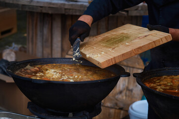 The chef adds garlic chopped on a cutting board to the meat soup with a knife. Boiling fresh food from vegetables and beef in a large cauldron. Catering and small business. Selective focus