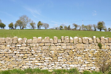 Old stone wall in the countryside with a green field and blue sky beyond
