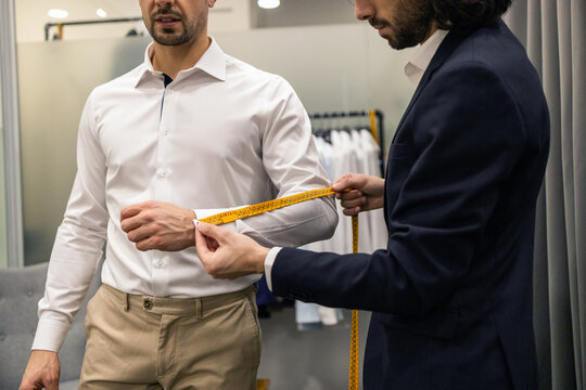 Tailor measuring a man sleeve for a custom shirt fitting in suit store