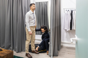 Tailor measuring man for clothing adjustments in a suit store