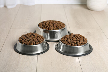Dry pet food in feeding bowls on floor indoors