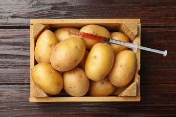 GMO concept. Potatoes in crate and syringe with liquid on wooden table, top view