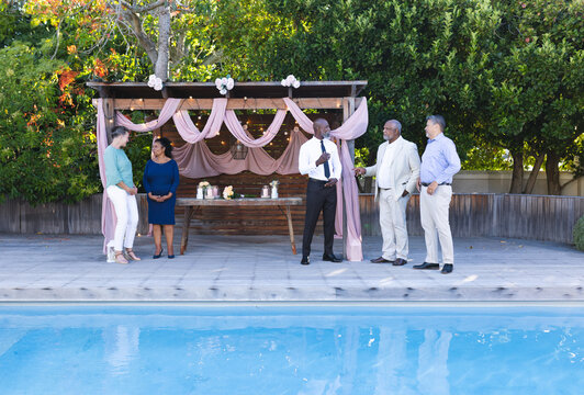 Celebrating by poolside, senior diverse friends in conversation and laughter in garden gathering