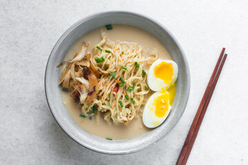 Overhead view of noodles in milk broth in a grey bowl, top view of ramen noodles in creamy chicken broth on a marble countertop