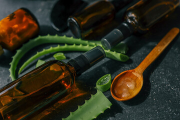 Close-up of fresh aloe vera slices and gel in a wooden spoon next to amber glass spray bottles on a...