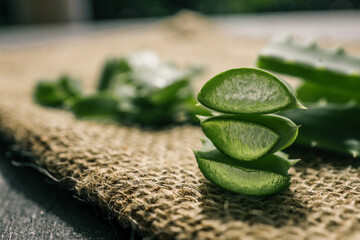 Stacked fresh aloe vera slices on a textured burlap surface. Transparent gel inside the leaves...