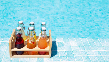 Close-up of a wooden box with glass bottles on the side of the pool. Delicious chilled multicolored...