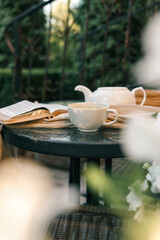 Cozy outdoor scene with a cup of tea, open book, teapot, and a soft scarf on a table. Warm and relaxing atmosphere, perfect for reading, relaxation, and enjoying peaceful moments in nature