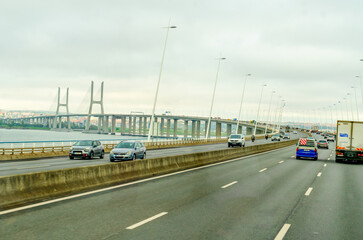 Lisbon, Portugal - October 31, 2024: Traffic on The Vasco da Gama Bridge (Portuguese: Ponte Vasco da Gama) is a cable-stayed bridge in a rainy day.