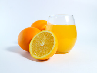 Fresh orange juice in a glass with whole and sliced oranges on a white background