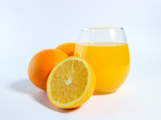 Fresh orange juice in a glass with whole and sliced oranges on a white background