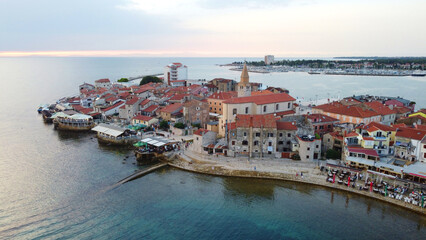 Aerial view, charming coastal town on the Adriatic Sea,  red-roofed stone buildings, a historic church with a bell tower, and a scenic waterfront promenade. European mediterranean destination.