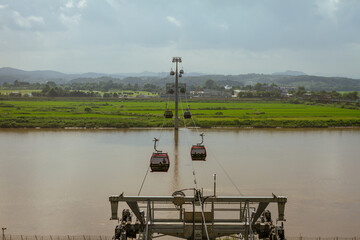 Scenic Cable Cars Gliding Over A Serene River With Green Fields And Rolling Hills In The Background