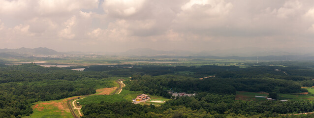Aerial View Of North Korea, Green Forests, Rolling Hills, And Rural Landscape With Winding Roads Under Cloudy Sky