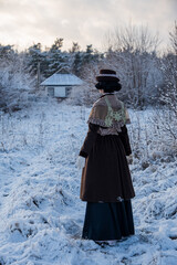Vintage fashion for winter, historic costume reconstruction. Brown wool coat with waist tight silhouette, shawl with laces on shoulders. Snowy track in the village. Poltava, Ukraine, 01/04/2025.