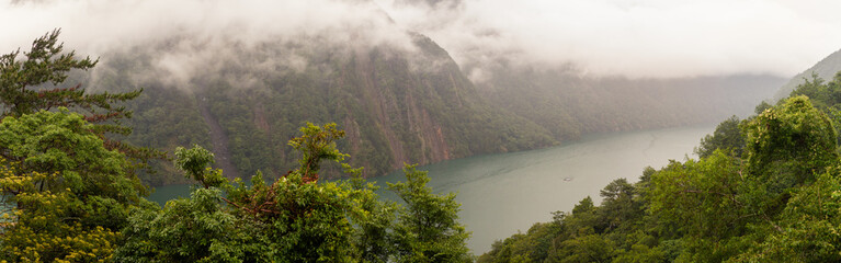 Misty Mountain Cliffs Towering Over Serene Emerald Lake Surrounded by Lush Greenery in Taiwan’s Remote Wilderness