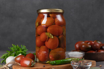 Homemade pickled tomatoes with chili peppers and parsley in jar on gray background