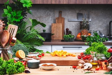Healthy eating, cooking, food blogging background. Sweet potato chopped into cubes on oak cutting board with vegetables, herbs and spices on cozy kitchen with wooden table, kitchenware 