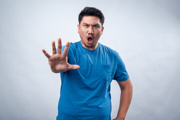 Fototapeta premium An Asian man in a blue t-shirt extends his hand forward with his palm open in a commanding 