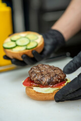 Chef in black gloves preparing gourmet burgers with fresh vegetables and sauce and cutlet in fast food restaurant