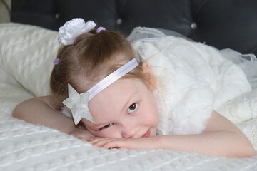 little baby sleeping in bed. small girl is laying on a sofa in a beautiful white dress with a silver star