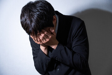 顔を手で隠すビジネスマンとスポットライト